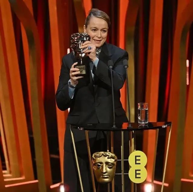 Actress Samantha Morton smiles behind a podium while holding up a golden BAFTA award trophy during an acceptance speech