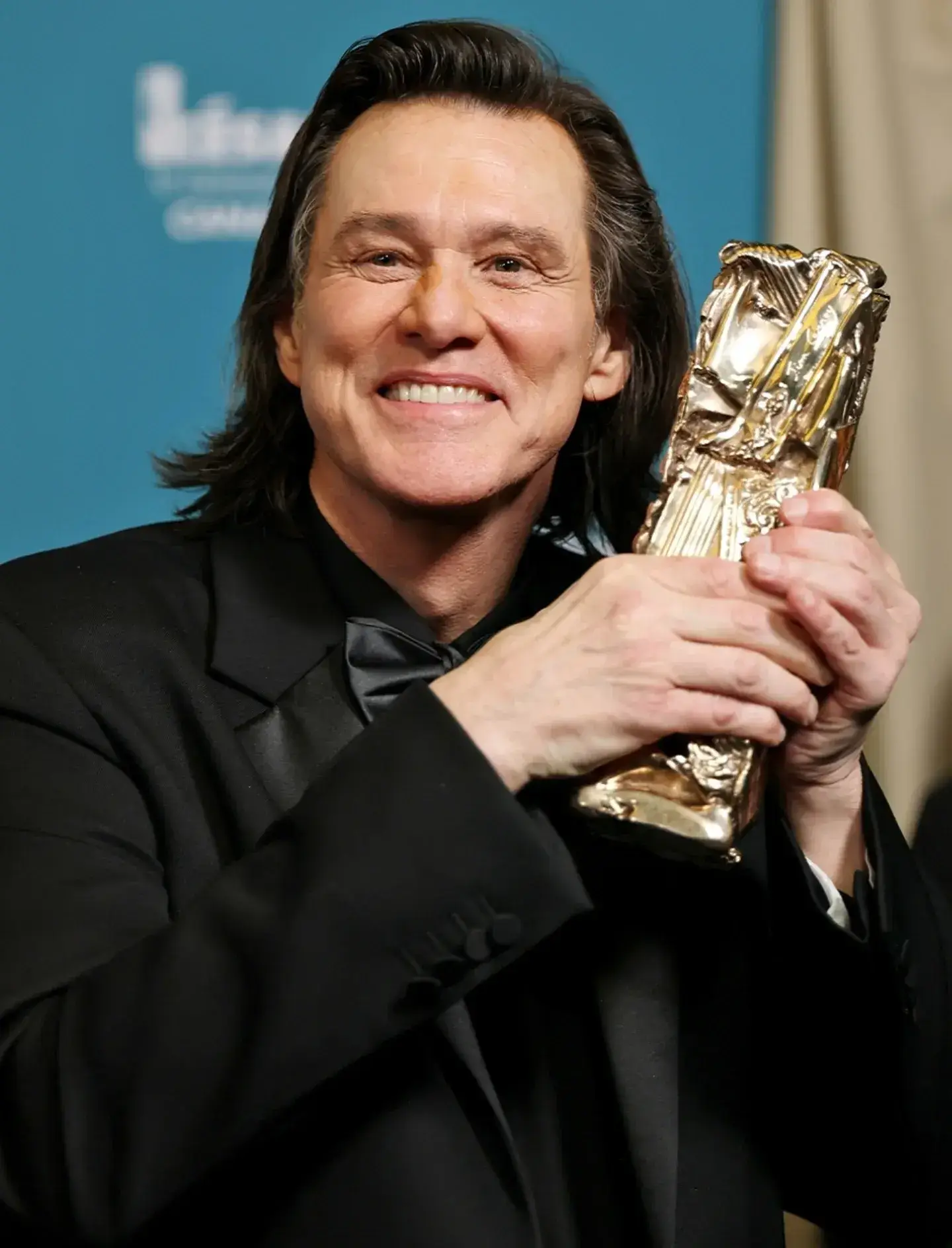 Jim Carrey holding his golden trophy near his face at the 51st Cesar Film Awards.