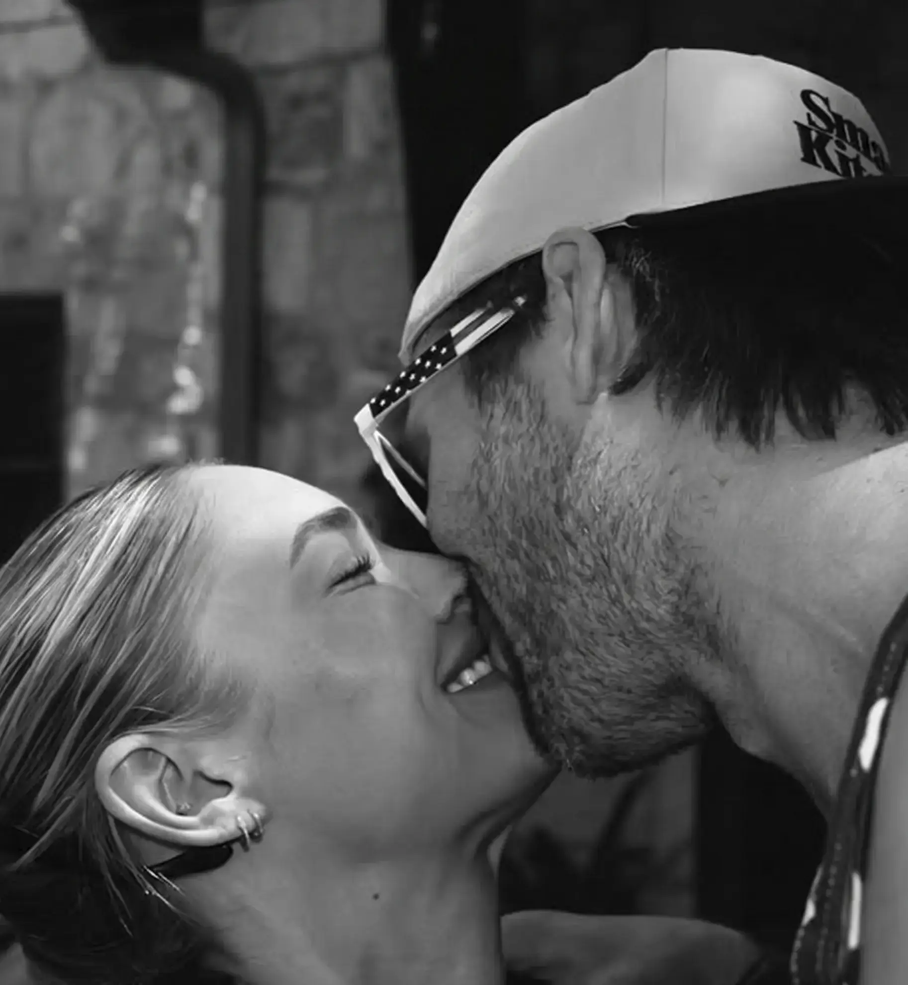 black and white photograph of Glen Powell and Michelle Randolph sharing a sweet kiss while smiling.