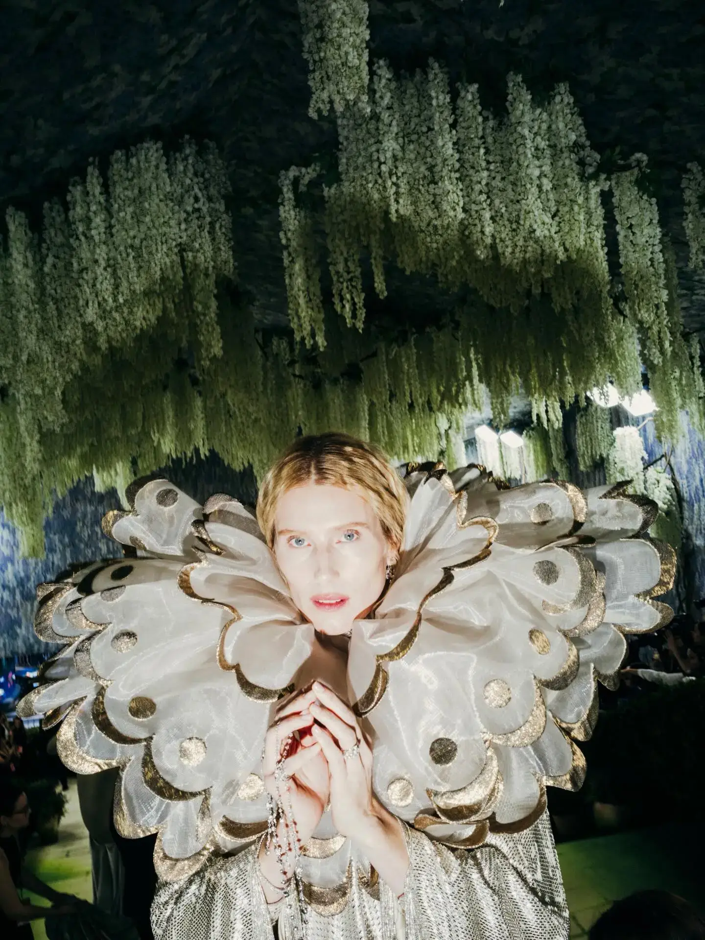 Model Dree Hemingway poses under hanging green wisteria while wearing an avant-garde Valentino gown with an oversized ruffled collar.