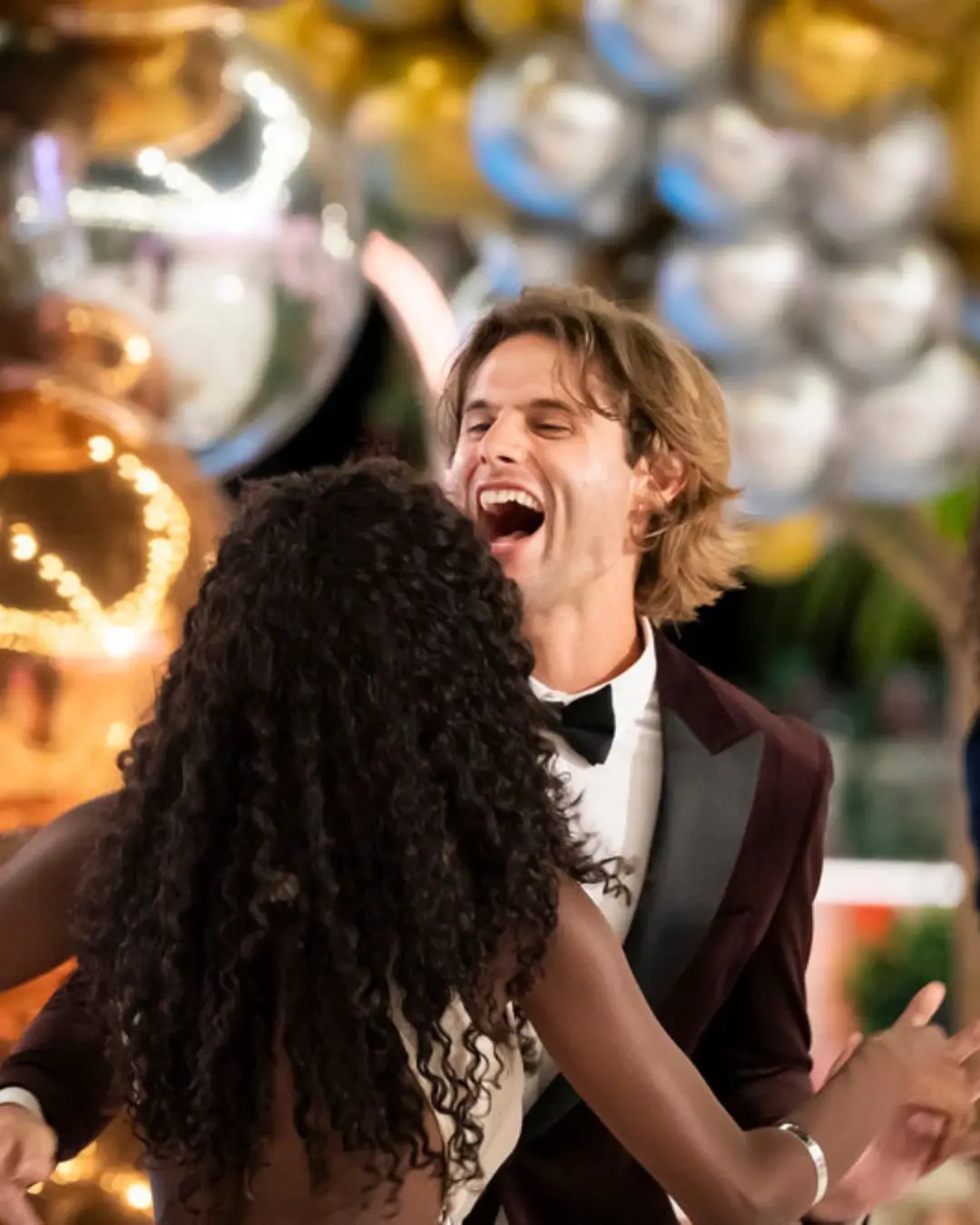 A joyful Bryce Dettloff laughs excitedly while embracing Trinity Tatum amidst festive gold and silver balloons at the Love Island USA Season 8 finale.