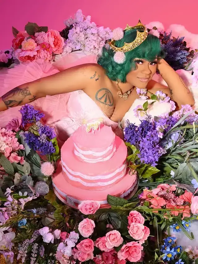 Singer Nivea lies among colorful flowers wearing a crown and a pink gown behind a multi-tiered pink birthday cake.