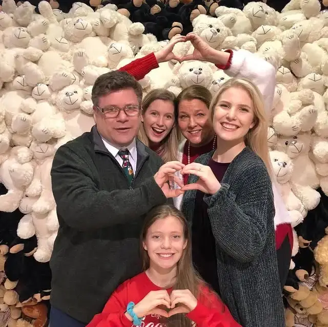 Sean Astin poses with his wife Christine and daughters Alexandra, Elizabeth, and Bella making hand hearts against a wall of teddy bears.