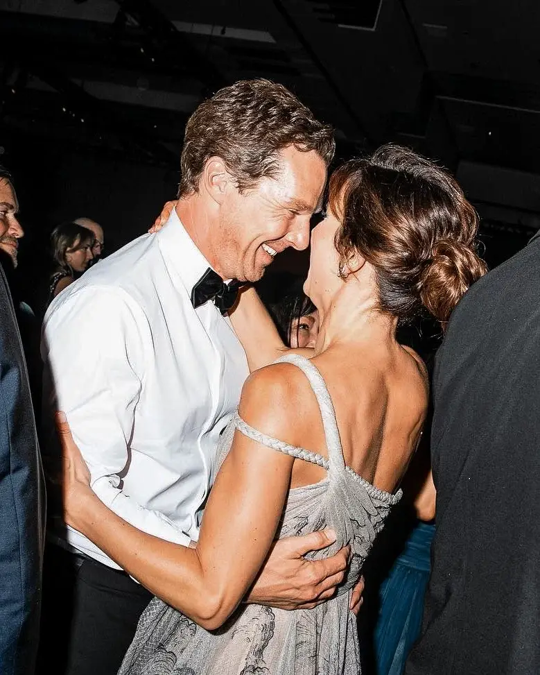 Benedict Cumberbatch and his wife Sophie Hunter embrace closely and smile at each other at an evening event.