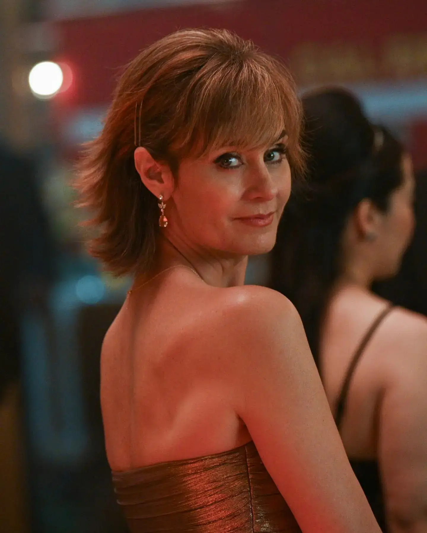Sharon Leone looking over her shoulder in a metallic strapless dress with a slight smile.