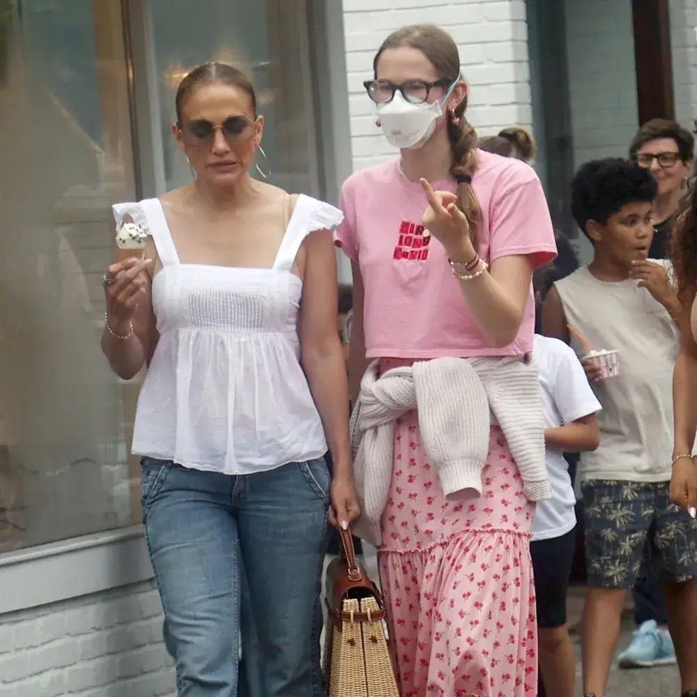 Jennifer Lopez in a white top eating ice cream while walking alongside stepdaughter Violet Affleck in a pink outfit and face mask.
