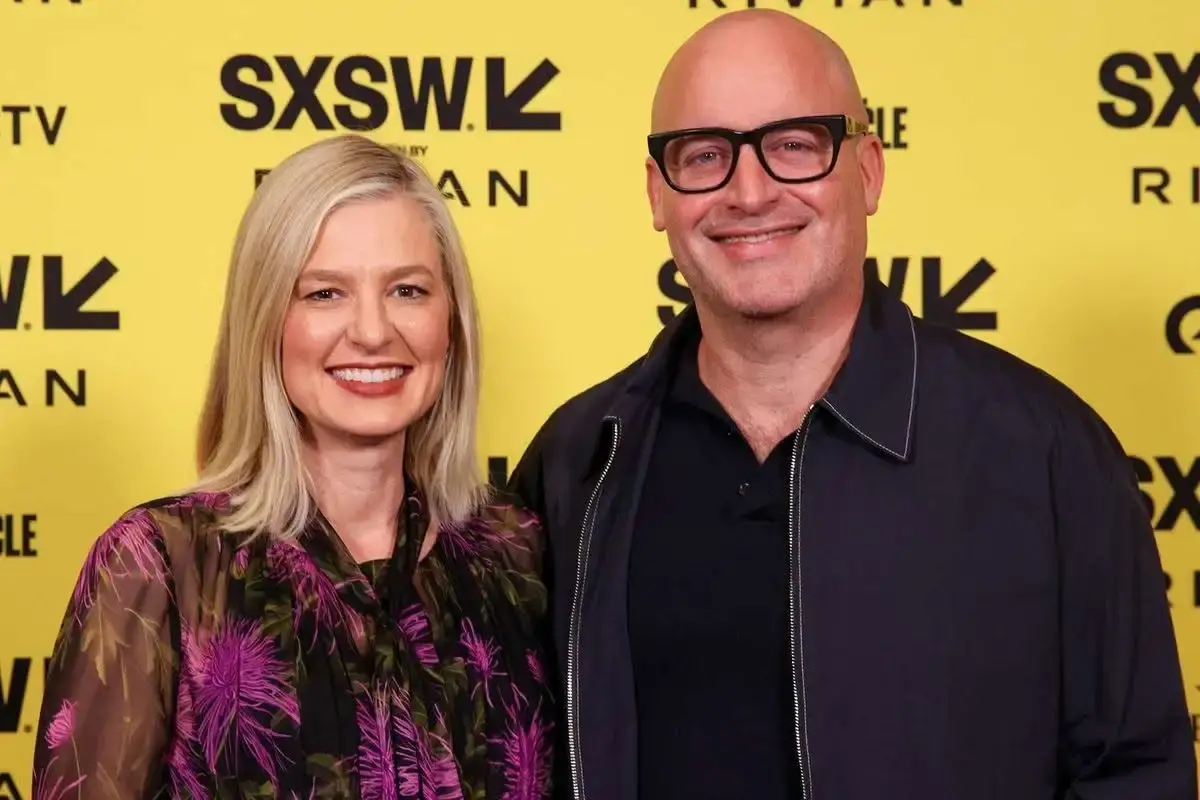 Christina Pazsitzky in a black patterned top and Tom Segura in a dark jacket pose together smiling in front of a yellow SXSW backdrop.