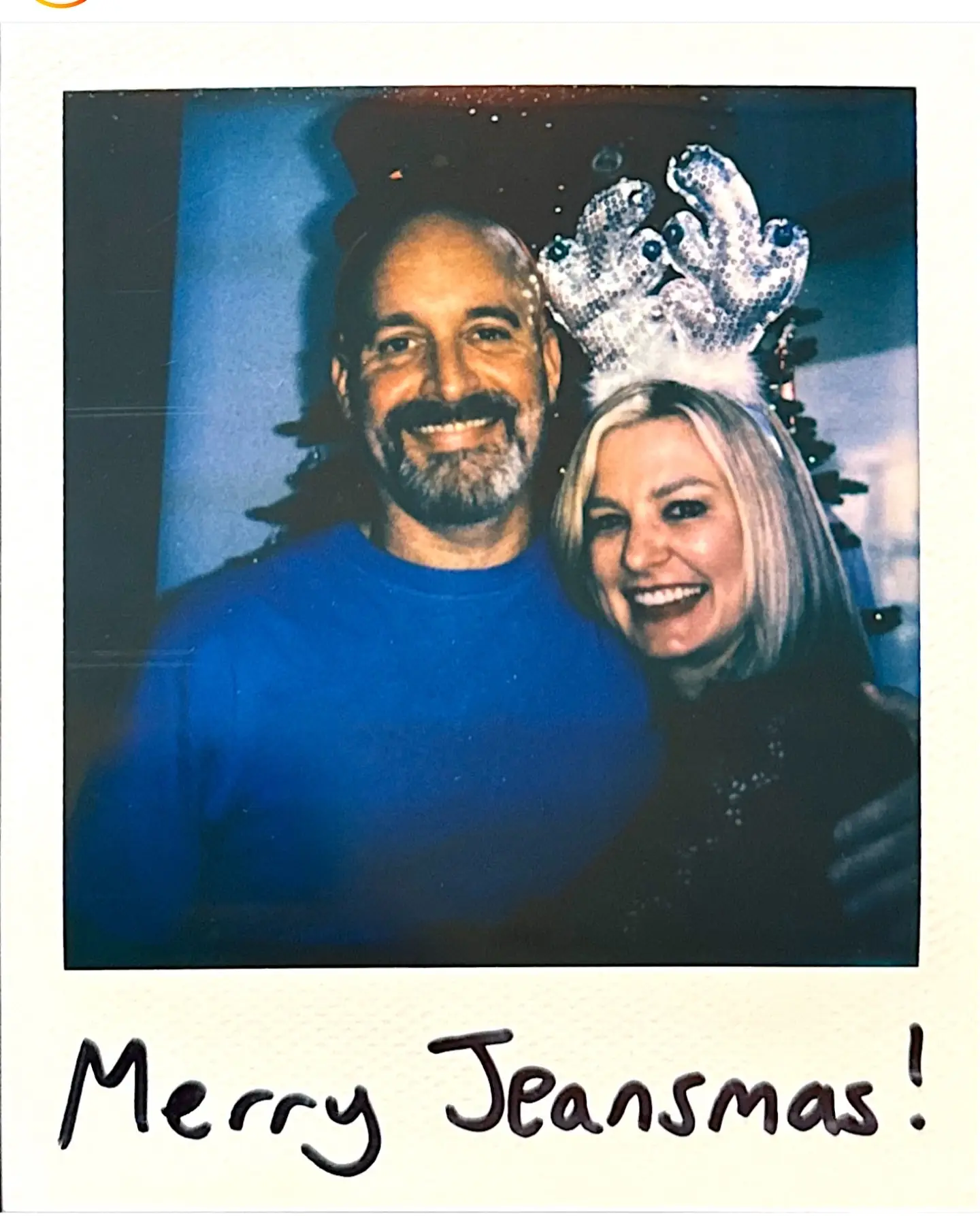 Polaroid picture of Tom Segura and his ex, Christina Pazsitzky wearing silver antlers, with handwritten text reading "Merry Jeansmas!" at the bottom.