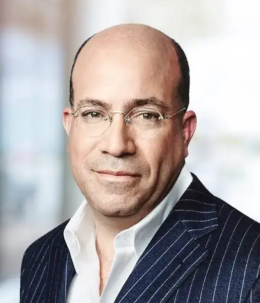 Headshot portrait of media executive Jeff Zucker wearing rimless glasses and a navy blue pinstripe suit jacket over an open-collar white shirt.