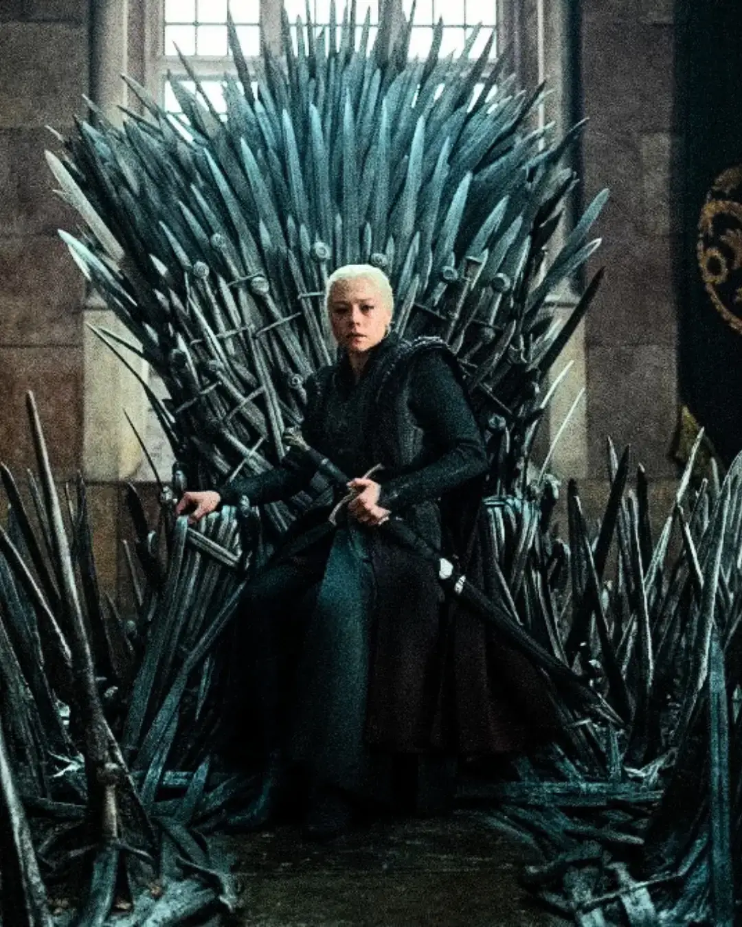Rhaenyra Targaryen sitting sternly on the Iron Throne in dark robes while holding a sword.