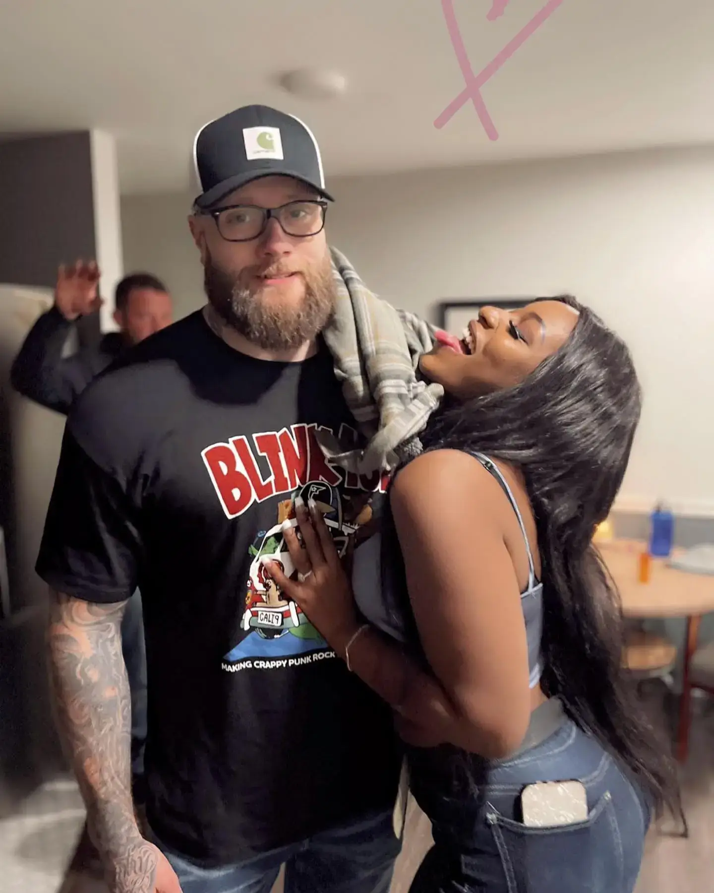 Dalton in a black graphic t-shirt and baseball cap standing next to Sako, who leans in playfully indoors.