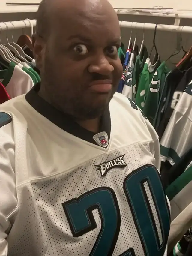Bryant Moreland, known as EDP445, wearing a white Philadelphia Eagles jersey while making an exaggerated facial expression in front of a closet filled with clothes.