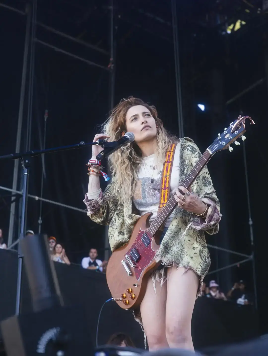 Paris Jackson playing an electric guitar and singing into a microphone on stage during a live concert performance.