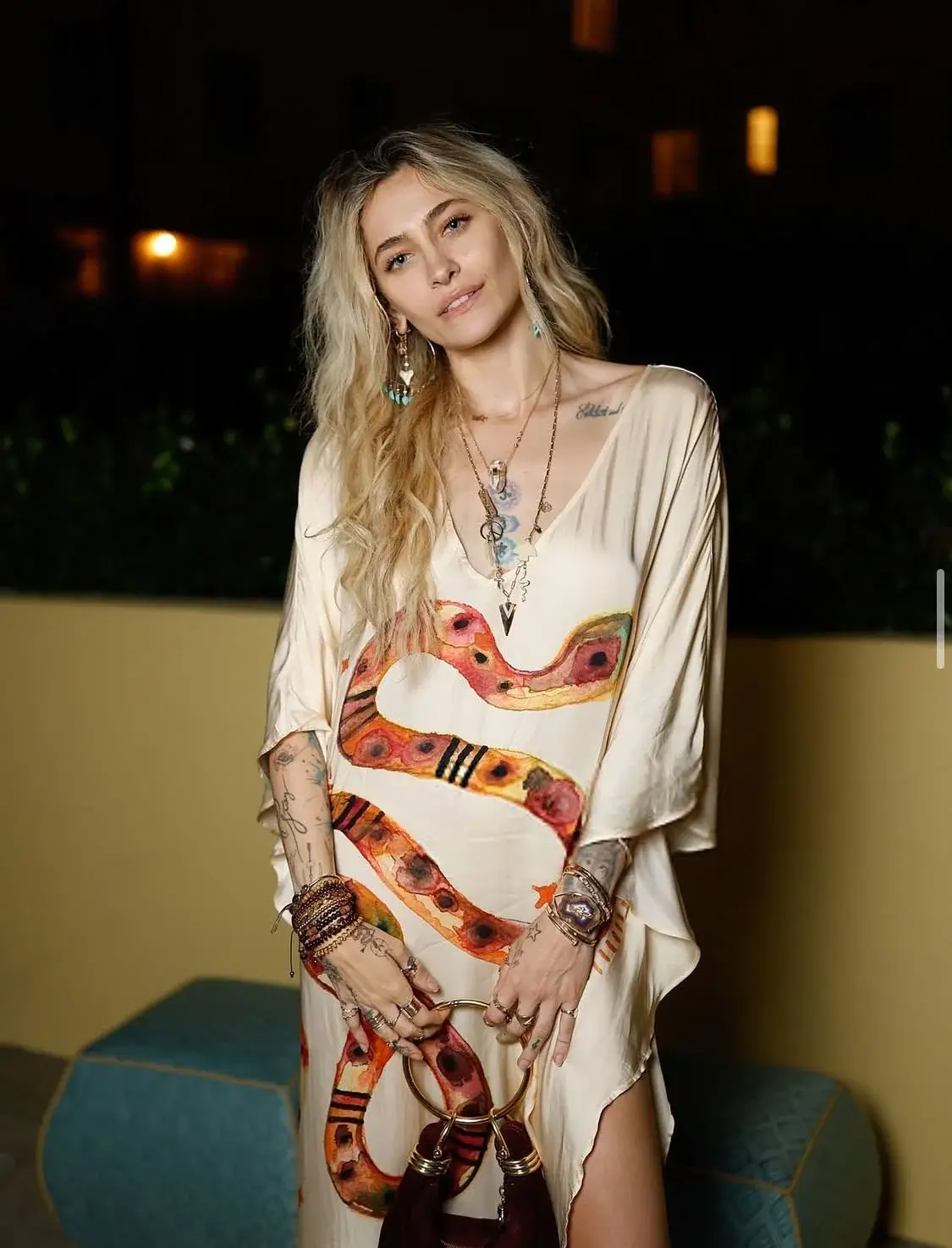 Paris Jackson with an orange snake print, layered bohemian jewelry, and a round-handled handbag.