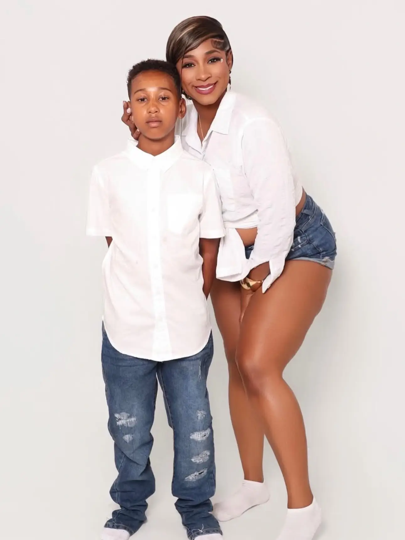 Karlissa Saffold wearing a white crop shirt and denim shorts poses standing beside her young son in a matching white button-up shirt