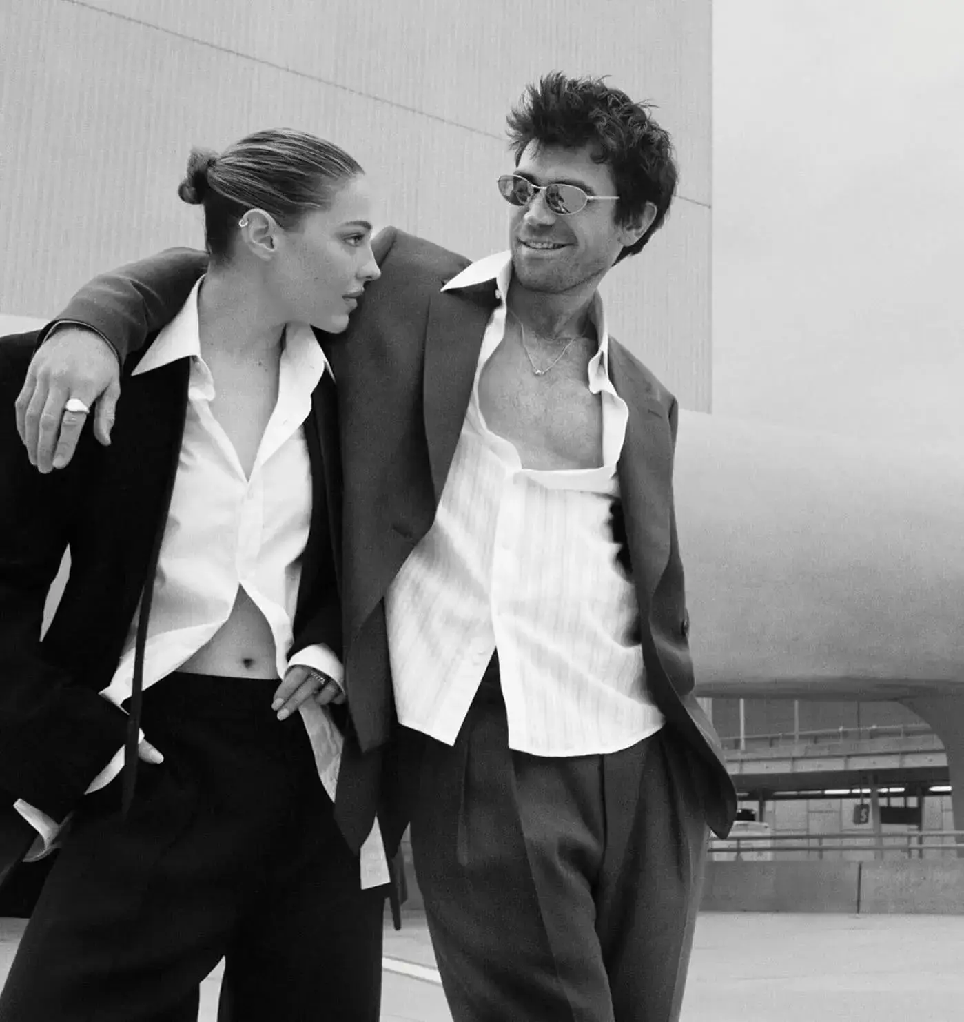 Madelyn Cline and KJ Apa posing together in a black-and-white photoshoot wearing coordinated oversized suits and unbuttoned shirts.