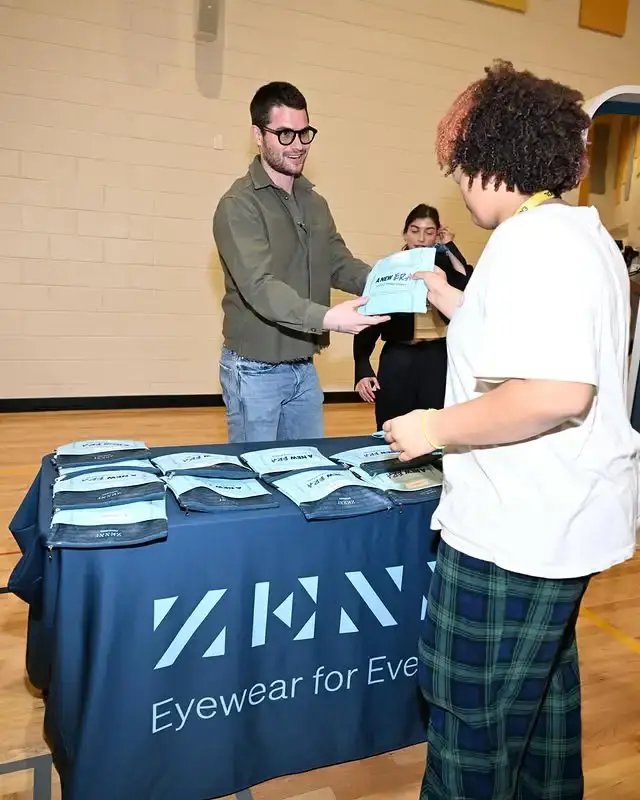 Chase Stokes handing out free eyeglasses pouches to a student at a Zenni Optical community charity event.