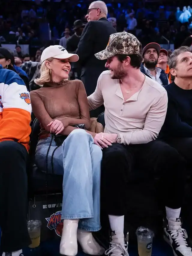 Chase Stokes and his ex-girlfriend Kelsea Ballerini laughing and holding hands while sitting courtside at a basketball game.