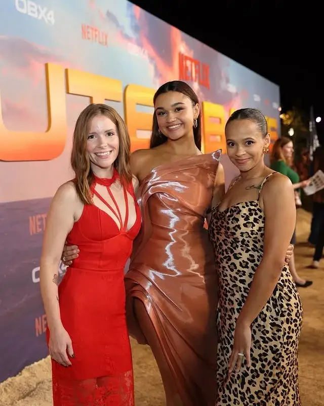 Madison Bailey in a metallic gown poses on the red carpet flanked by Katie Harden in red and Kristina Norine Chapman in a leopard print dress.