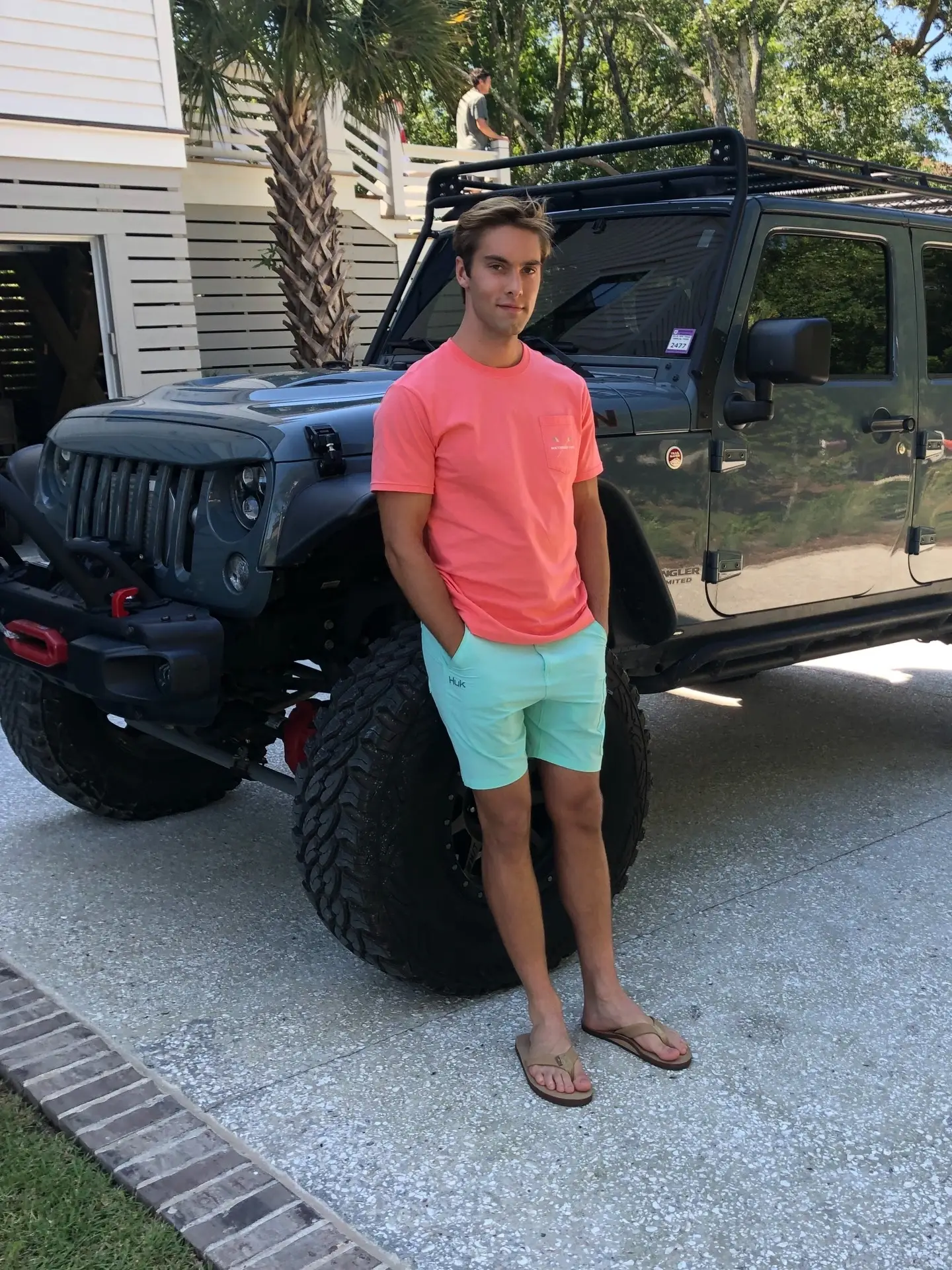 Austin North posing full-length in a coral t-shirt and mint green shorts leaning against a grey Jeep.