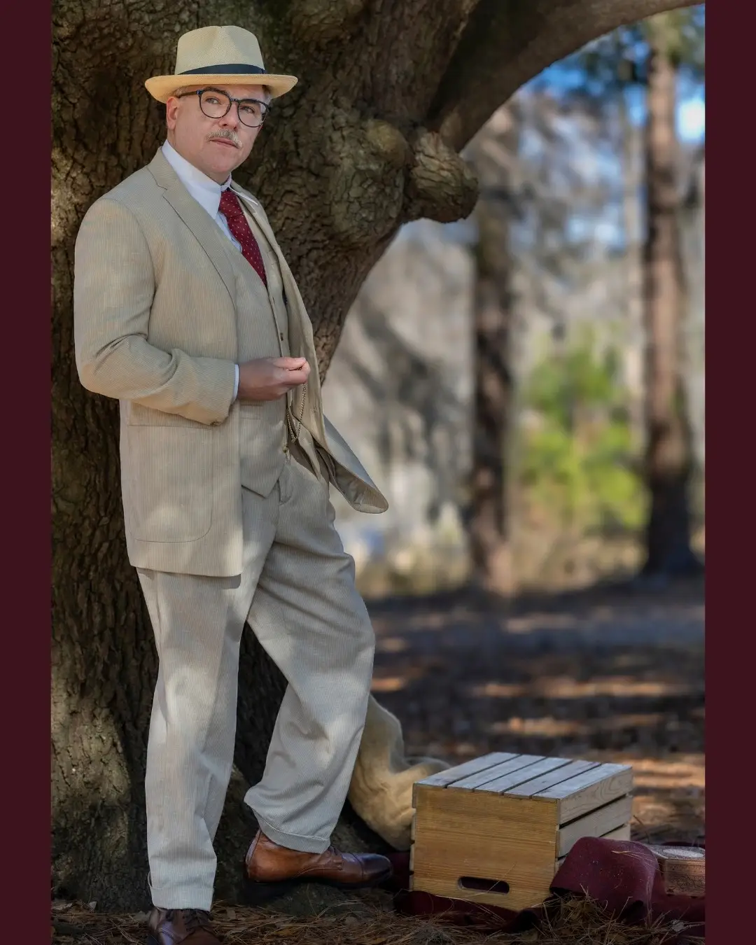 Cullen Moss posing full-length in a beige vintage three-piece suit and straw fedora hat while leaning against a large tree.