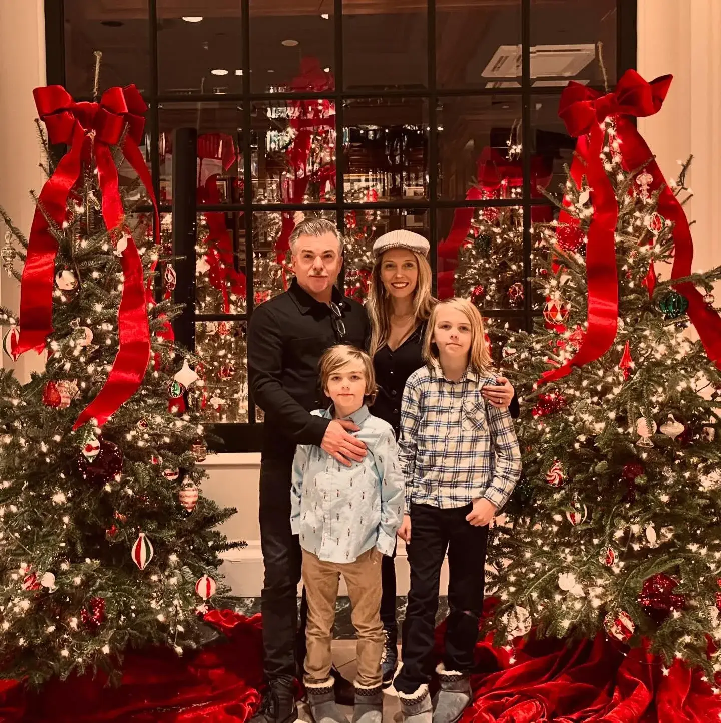 Cullen Moss and his wife Madison Moss pose with their two children between decorated Christmas trees with large red bows.
