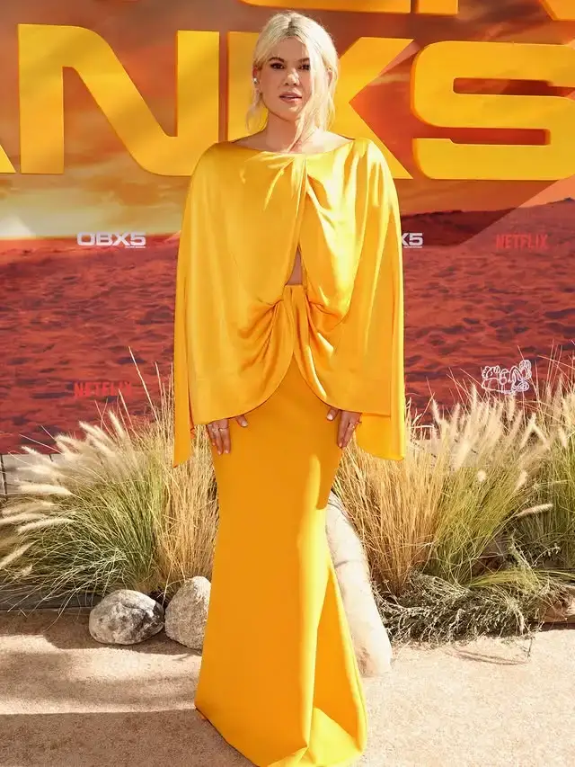 Caroline Arapoglou posing full-length in an elegant draped bright yellow gown on the Outer Banks red carpet.