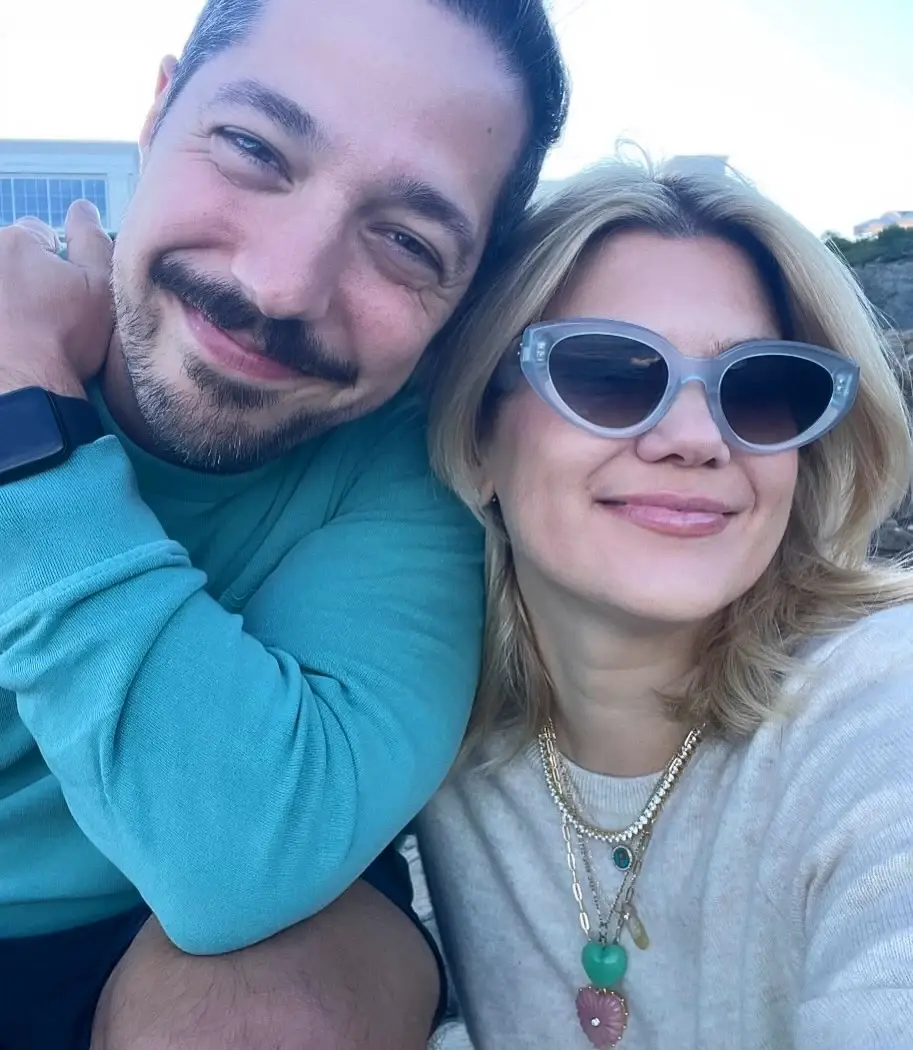 Caroline Arapoglou and her husband Nick Arapoglou smiling warmly together during a sunny outdoor selfie.