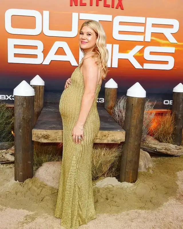 Caroline Arapoglou posing in a sparkling gold ribbed gown at the Outer Banks red carpet premiere.