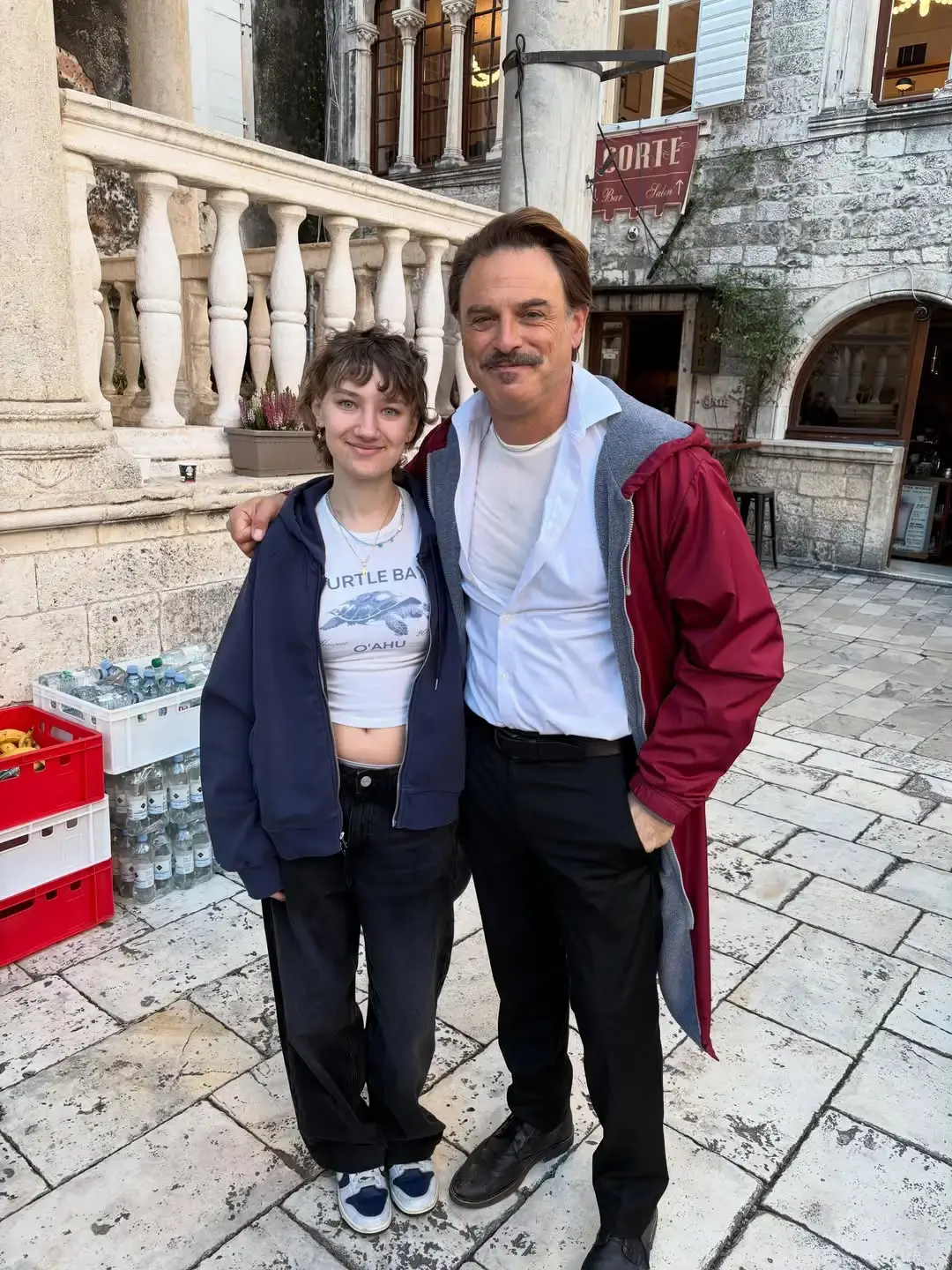 Amelie standing outdoors alongside J. Anthony Crane in front of a stone building terrace.