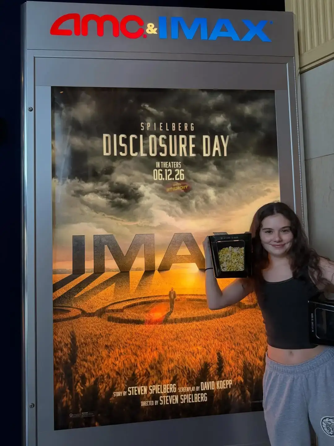 Julia Antonelli smiling and holding a container of popcorn next to a large IMAX theater movie poster.