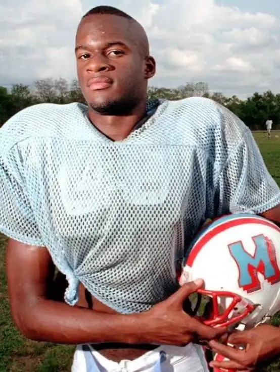 Vince Young as a young high school football player holding his helmet on the field in a practice jersey.