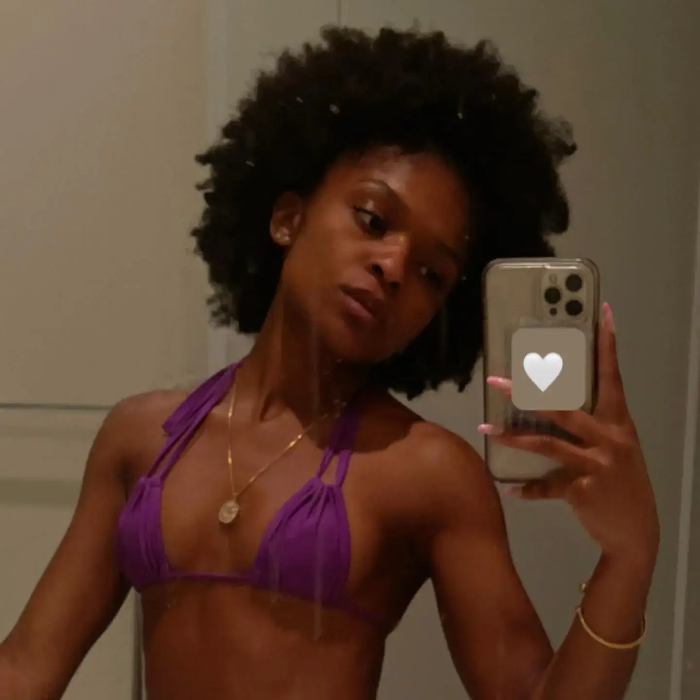 Dominique Thorne taking a mirror selfie wearing a purple bikini top with natural afro hairstyle.