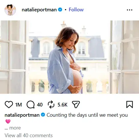 Natalie Portman cradling her bare baby bump by an open balcony window while wearing an unbuttoned blue oversized shirt.