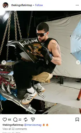 Bad Bunny wearing sunglasses and reading Interview Magazine while seated on an engine prop in a studio.
