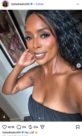 Tasha Smith smiling warmly with wavy dark hair and glowing makeup in a strapless black top.