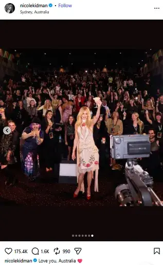 Nicole Kidman holding up a drink while standing in an embroidered dress in front of a packed movie theater audience in Sydney.
