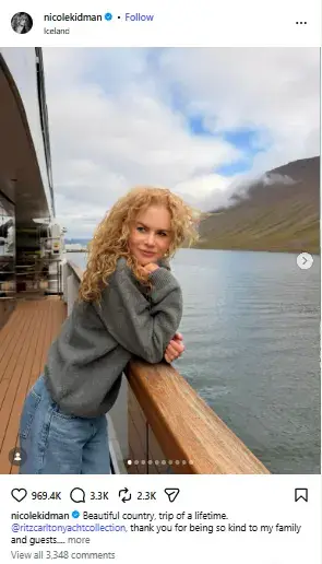 Nicole Kidman leaning on the wooden railing of a yacht with curly hair and a gray sweater against scenic Icelandic waters.