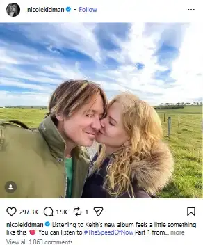 Nicole Kidman kissing Keith Urban on the cheek outdoors in a grassy rural landscape under a partly cloudy sky.