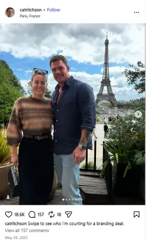 Alan Ritchson and Catherine smiling together on a scenic terrace overlooking the Eiffel Tower in Paris.