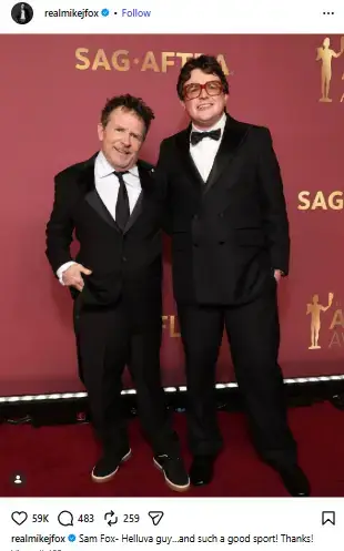 Michael J. Fox and his son Sam Fox smiling together in black suits and ties on the red carpet at the SAG-AFTRA Awards.
