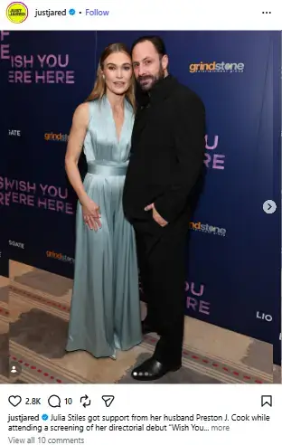 Julia Stiles in a light blue satin jumpsuit posing alongside her husband Preston J. Cook against an event backdrop.