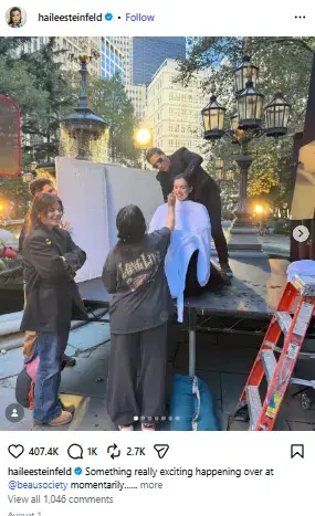Hailee Steinfeld getting hair and makeup touch-ups from her styling crew while sitting on an outdoor production set.