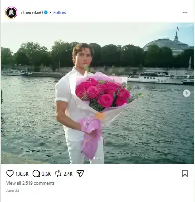 Braden Peters dressed in an all-white outfit holding a large bouquet of pink roses beside a scenic river waterfront.