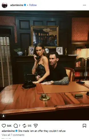 Behati Prinsloo holding a vintage telephone while posing beside Adam Levine seated at a classic wooden executive desk.