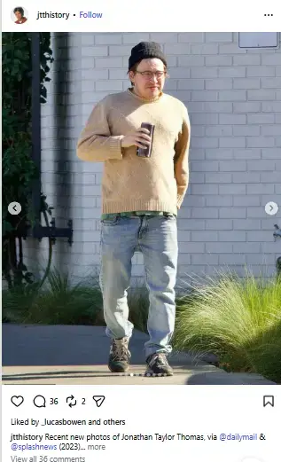Jonathan Taylor Thomas in a beige sweater, black beanie, and jeans walking outside with a drink in hand.