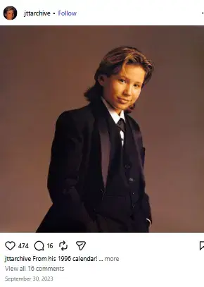 Young Jonathan Taylor Thomas posing in a black formal suit and tie with hands in his pockets against a brown backdrop.