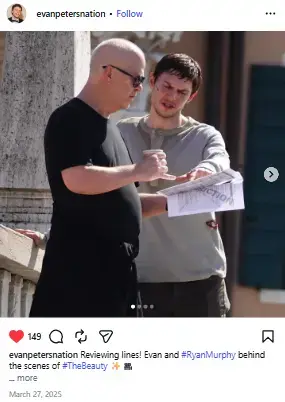 Ryan Murphy in sunglasses and Evan Peters holding a coffee cup review a script paper outdoors on set.
