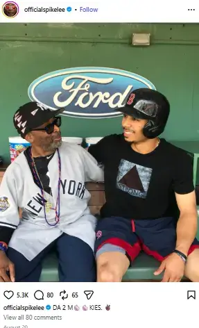 Spike Lee in a New York Yankees jersey sitting in a dugout alongside MLB star Mookie Betts wearing a Red Sox batting helmet.