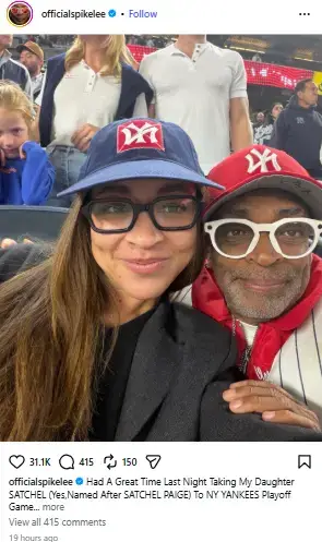 Spike Lee and his daughter Satchel posing together in the stands wearing matching New York Yankees baseball caps and glasses.
